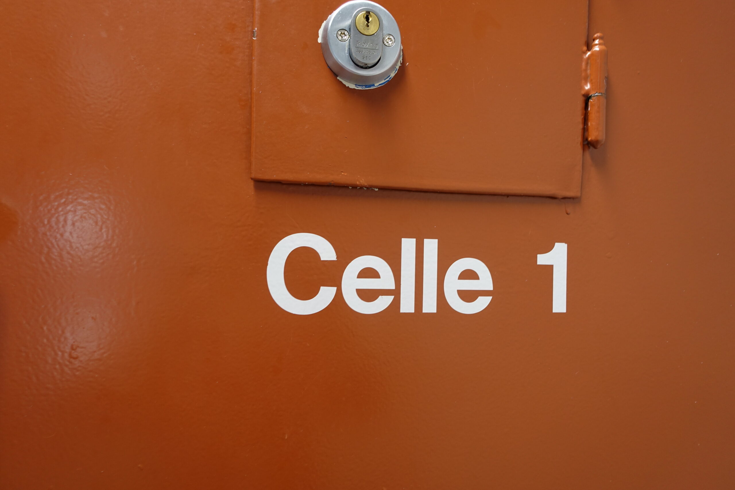 Oransje vegg med "Celle 12 i hvit skrift og luke rett over