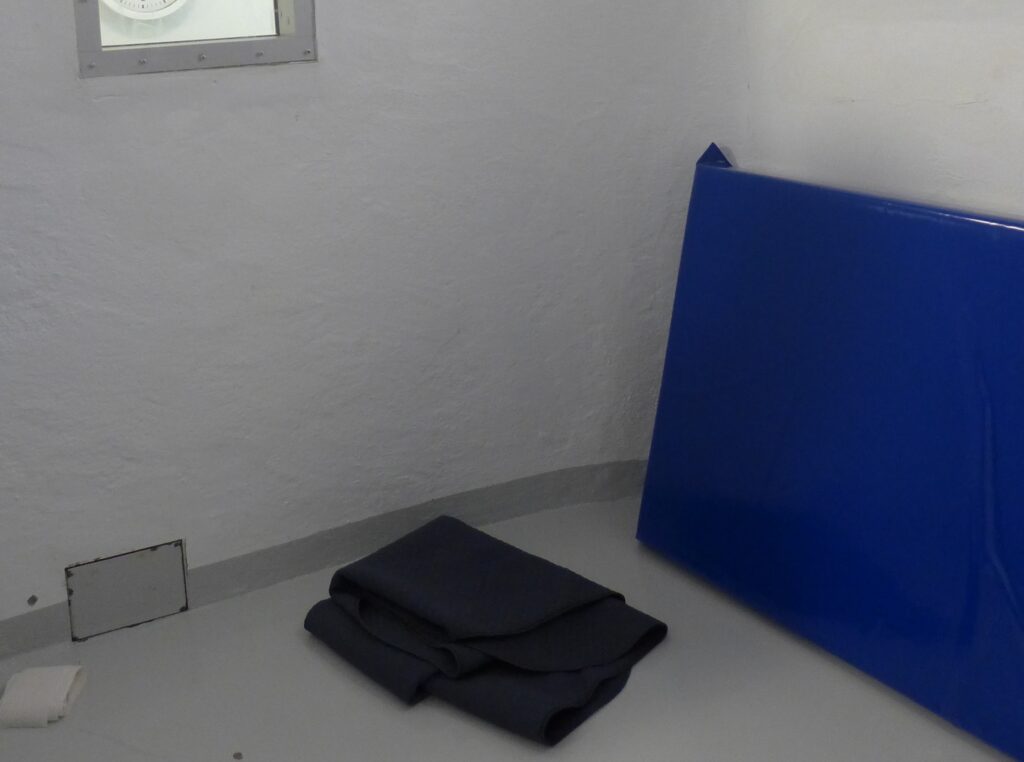 Innsiden av en celle med blå plastmadrass opp langs veggen